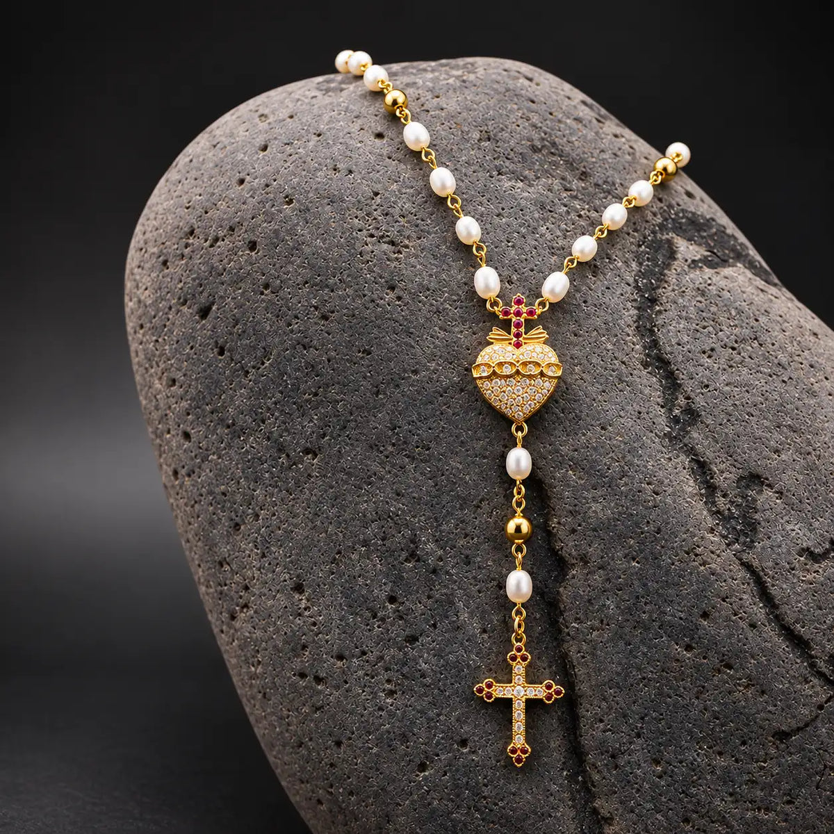 Terço Mi Corazon com pérolas e Coração Vaticano em prata dourada, apresentado sobre pedra escura.