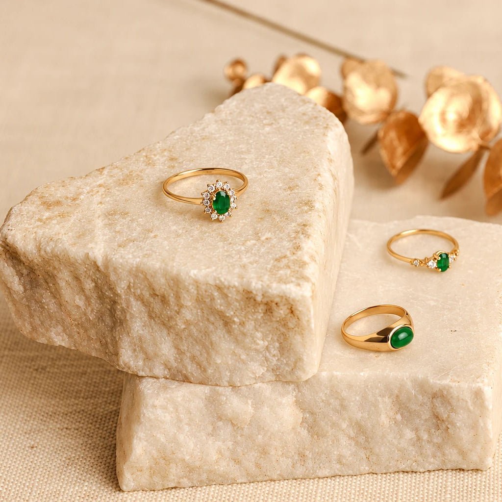 Anel chuveiro em ouro de 19kl com pedra verde e zircónias, junto a outros anéis sobre blocos de pedra clara