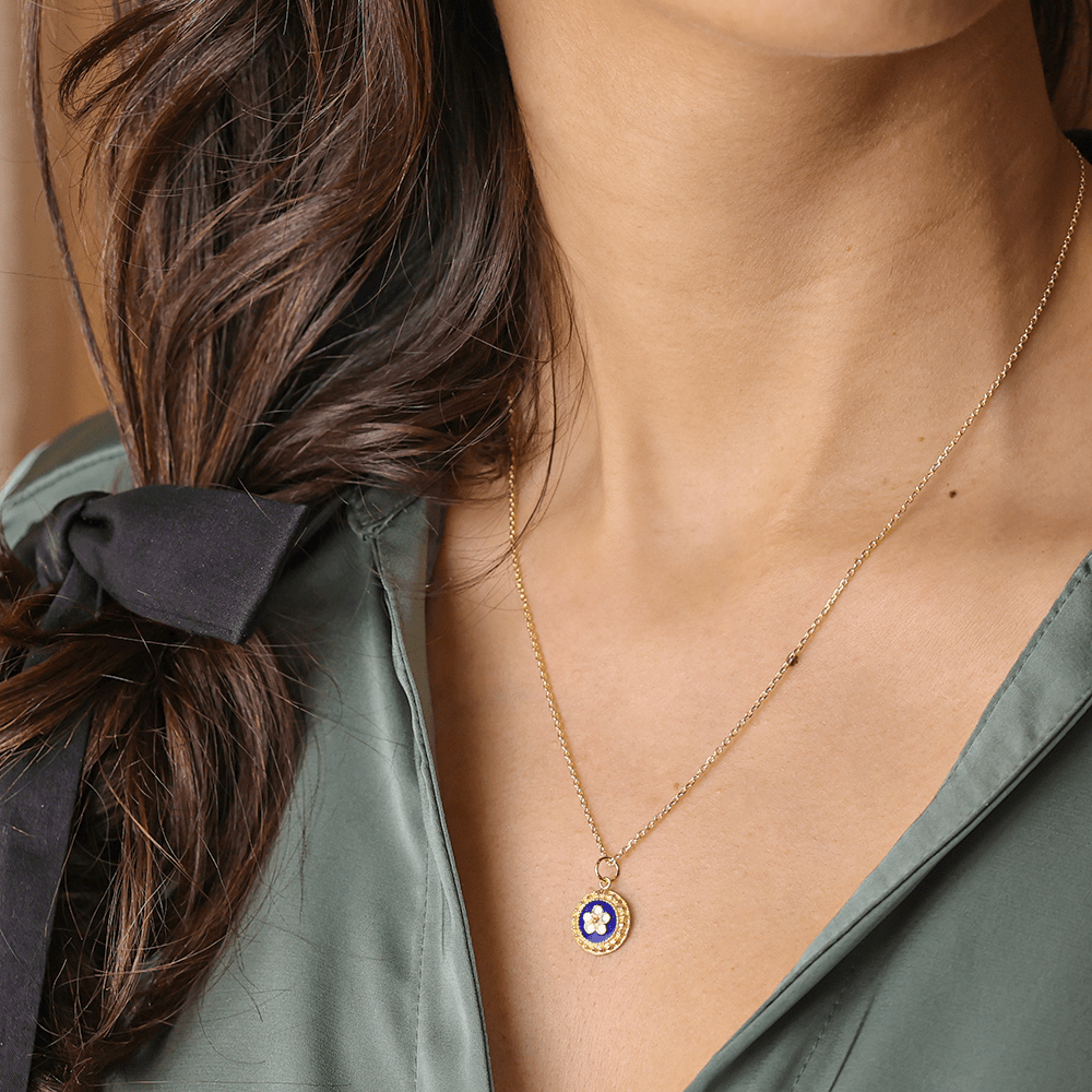 Medalha circular com motivos de caramujos e detalhes em esmalte azul e branco num fio dourado.