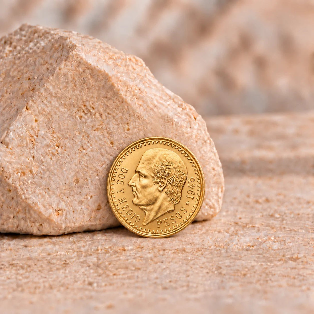Moeda de 2,5 pesos mexicanos em ouro, com retrato de perfil, apoiada numa pedra clara